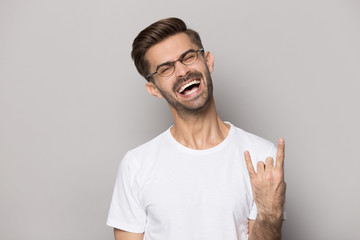 Crazy funny happy millennial guy in eyeglasses showing rock-n-roll gesture.