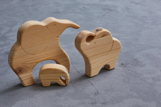 Wooden Toys. A family of 3 elephants carved in a jigsaw on a gray concrete background. Symbol of a happy strong family