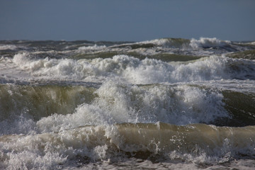 Waves of the north sea with white spindrift in front of a blue sky