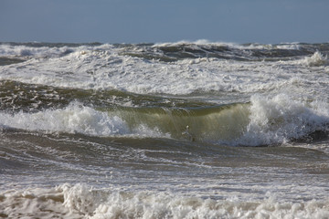 Waves of the north sea with white spindrift in front of a blue sky