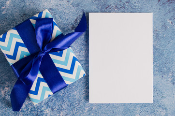 Greeting card for Father's Day or Birthday. Gift box with blank white paper on blue background.