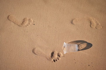 Footprints and plastic cup on a sandy beach, conceptual picture.