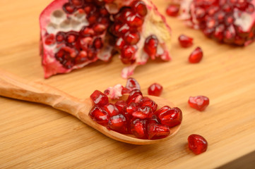 Chunks of ripe juicy pomegranate and pomegranate seeds on a wooden spoon on a wooden background. Close up.