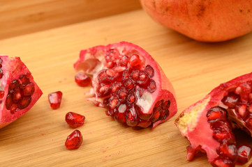Ripe juicy pomegranate and pieces of pomegranate on a wooden background. Close up.