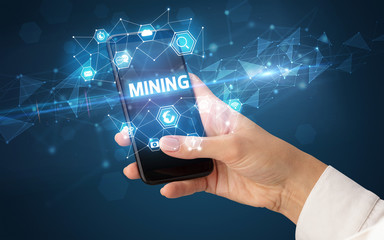 Female hand holding smartphone with MINING inscription, modern technology concept