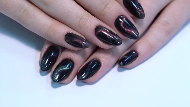 Closeup top view of professional colorful glossy brilliant holiday manicure at fingers of young woman. Modern trendy shiny amazing cat eye effect nail design. Real time 4k video footage.