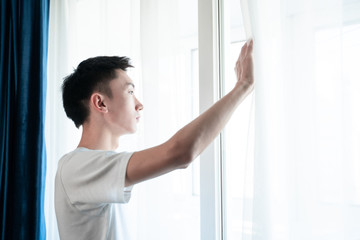 Chinese young man open curtain in bedroom in the morning