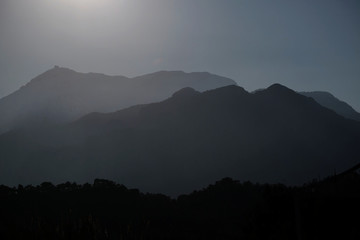 Нigh mountain silhouettes in haze with stepped lighting in backlight in the evening