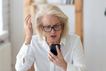 Mature businesswoman holding smartphone feels indignant having wi-fi connection problem