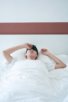 asian young man sleeping in bed with an eye mask in bedroom