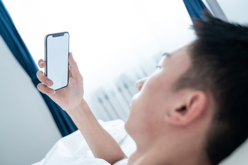 Attractive young man using a smartphone and texting while lying on his bed