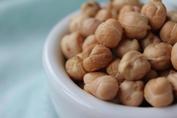 Close up view of a white bowl filled with chick peas (Cicer arietinum), on a wooden table with mint green table cloth. With copyspace.