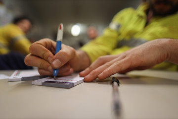 Construction high risk workers are writing personal safety risk assessment to minimise the risk prior working of each task with defocused co-worker sitting the chair at background