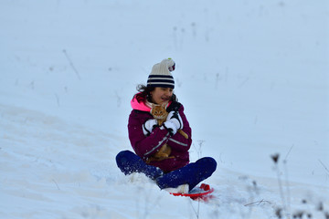Fototapeta na wymiar Girl sledding downhill on snow in winter and laughing with joy