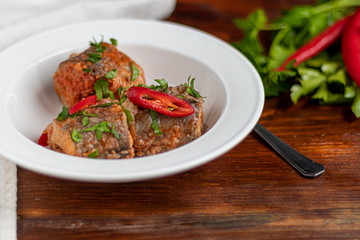 Cod fillet or other fish on a white plate. Braised in tomato and onion. Peas are sprinkled with green leaves and microgreen from seedlings. On a wooden background.