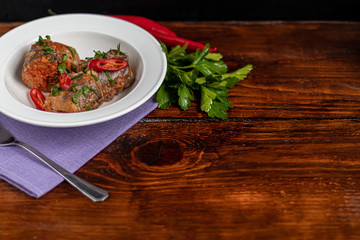 Cod fillet or other fish on a white plate. Braised in tomato and onion. Peas are sprinkled with green leaves and microgreen from seedlings. On a wooden background.
