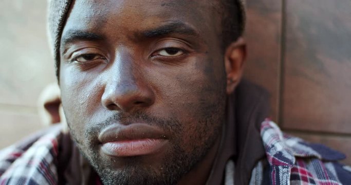 Close up of the face of young African American homeless man beggar looking straight to the camera with desperate eyes. Outdoor. Portrait.