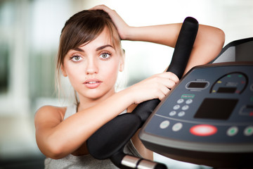 Portrait of young beautiful woman in sportswear standing near treadmill and looking at camera in gym. Healthy active lifestyle, sport, bodycare concept