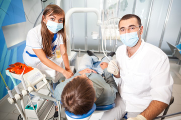 Fototapeta na wymiar Young dentist doctor man in white uniform and special mask and young nurse woman examining man patient in dental office in clinic. Dental health and medical care concept
