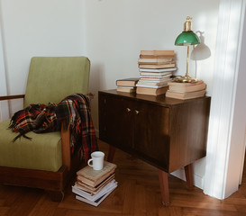 Antique bureau with old books and green lamp, armchair with wool plaid