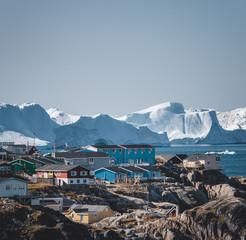 Aerial View of Arctic city of Ilulissat, Greenland. Colorful houses in the center of the town with icebergs in the background in summer on a sunny day with blue sky and clouds