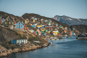 Colorful houses dot the hillsides of the fishing town of Kangaamiut, West Greenland. Icebergs from Kangia glacier in Greenland swimming with blue sky and clouds. Symbol of global warming. - obrazy, fototapety, plakaty
