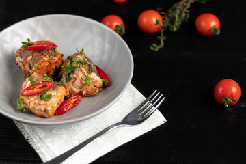 Cod filet or other fish on a gray plate. Braised in tomato and onion. Peas are sprinkled with green leaves and microgreen from seedlings. On a black wooden background.