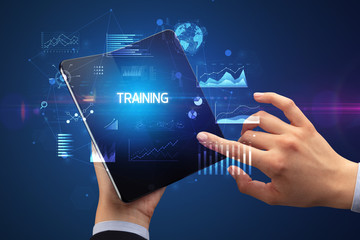 Businessman holding a foldable smartphone with TRAINING inscription, successful business concept