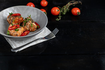 Cod filet or other fish on a gray plate. Braised in tomato and onion. Peas are sprinkled with green leaves and microgreen from seedlings. On a black wooden background.