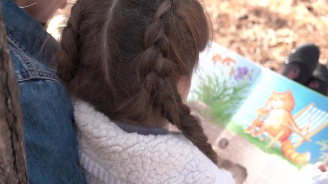 A young girl reads a children's book, a frame from behind