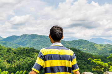 A Chinese tourist looking at the landscape of mountain and green forest under sunlight near Kandy, Sri Lanka.