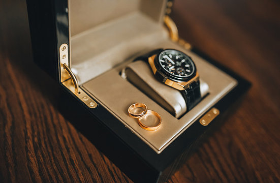 Wedding engagement gold rings in a box, case with an expensive watch close-up. Wedding accessories, details. The morning of the groom. Photography, concept.