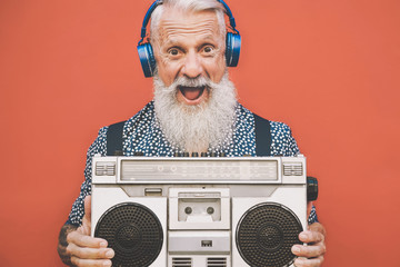 Happy senior man listening to music with boombox and headphones outdoor - Crazy hipster male having fun with vintage stereo - Concept of elderly people lifestyle