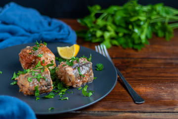 Cod filet or other fish on a gray plate. Braised in tomato and onion. Peas are sprinkled with green leaves and microgreen from seedlings.