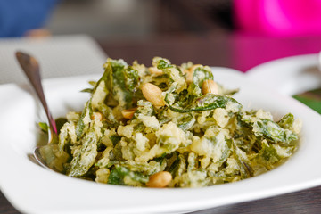 Close up view of crunchy Fried fresh tea leaves with peanut on white plate.