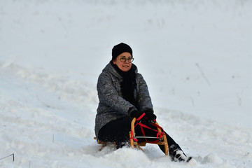 Fototapeta na wymiar Woman sledding downhill on snow in winter and laughing with domestic cat in her arms 