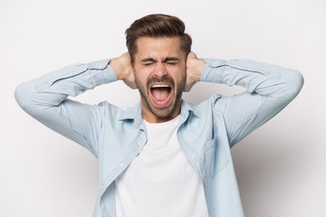 Annoyed young man covering ears with hands shouting, refusing listening.