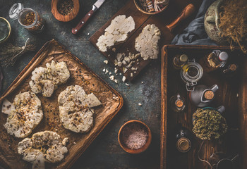 Vegan food cooking preparation. Cauliflower steaks on baking sheet  on rustic background with ingredients. Top view