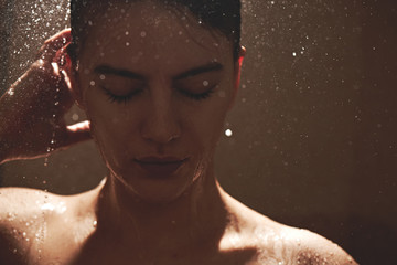 Girl in the shower under stream of water washes her hair, wet face close-up, enjoys eyes closed