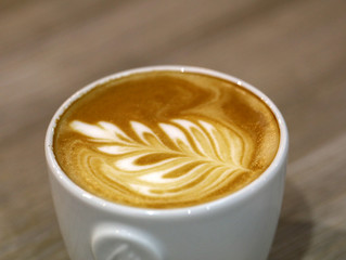The coffee barista poured milk into the coffee and created a beautiful leaf.