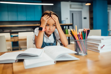 Portrait of unhappy little girl children tired after lesson in classroom.