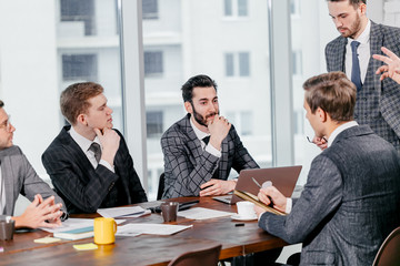 group of young business men gathered together to discuss business strategies and new ideas, business coworking in modern executive boardroom, everyone in stylish elegant tuxedo