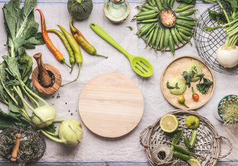 Fresh green food cooking concept. Various seasonal vegetables on table with kitchen tools and spoon , top view. Round wooden cutting board copy space. Healthy organic food. Paleo dieting. Vegetarian