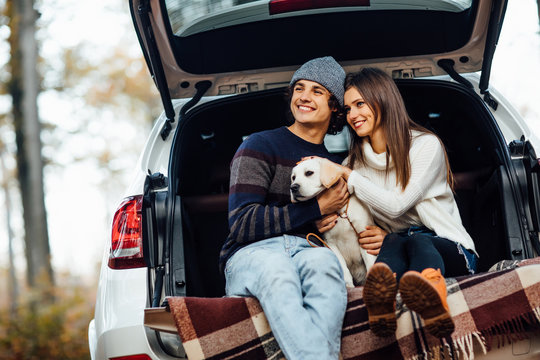 Young couple have a weekend time with their labrador retriver sitting in car in the autumn forest.