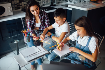 Happy mother and their adorable children doing homework, mother help them.