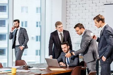 teamwork of young business men gathered in modern office with big panoramic window, everyone in formal suits, tuxedo. active discussion of projects and finance of company