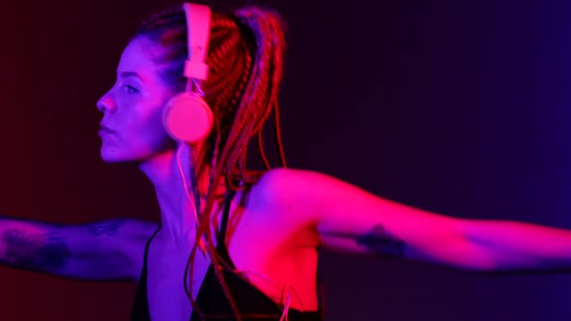 Footage of Dj woman with tree braids, dancing with headphones. With blue and red color lights. The video can be united with my other dj woman footages. Woman Makes different figures