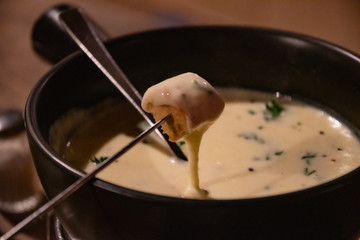 Traditional French cheese fondue in crockery black pot. Melted cheese on piece of grilled bread....