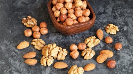 different types of nuts around a wooden dish with hazelnuts on a black background