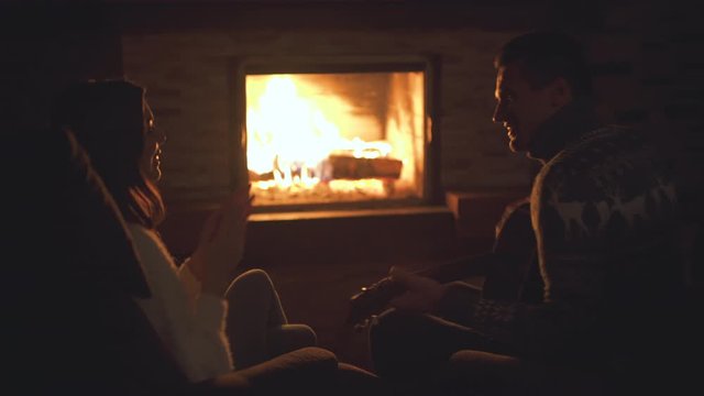 The man with woman playing guitar near the fireplace
